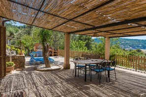 Une terrasse extérieure dotée d’un toit en bambou, d’une table avec des chaises et offrant une vue sur un paysage montagneux.