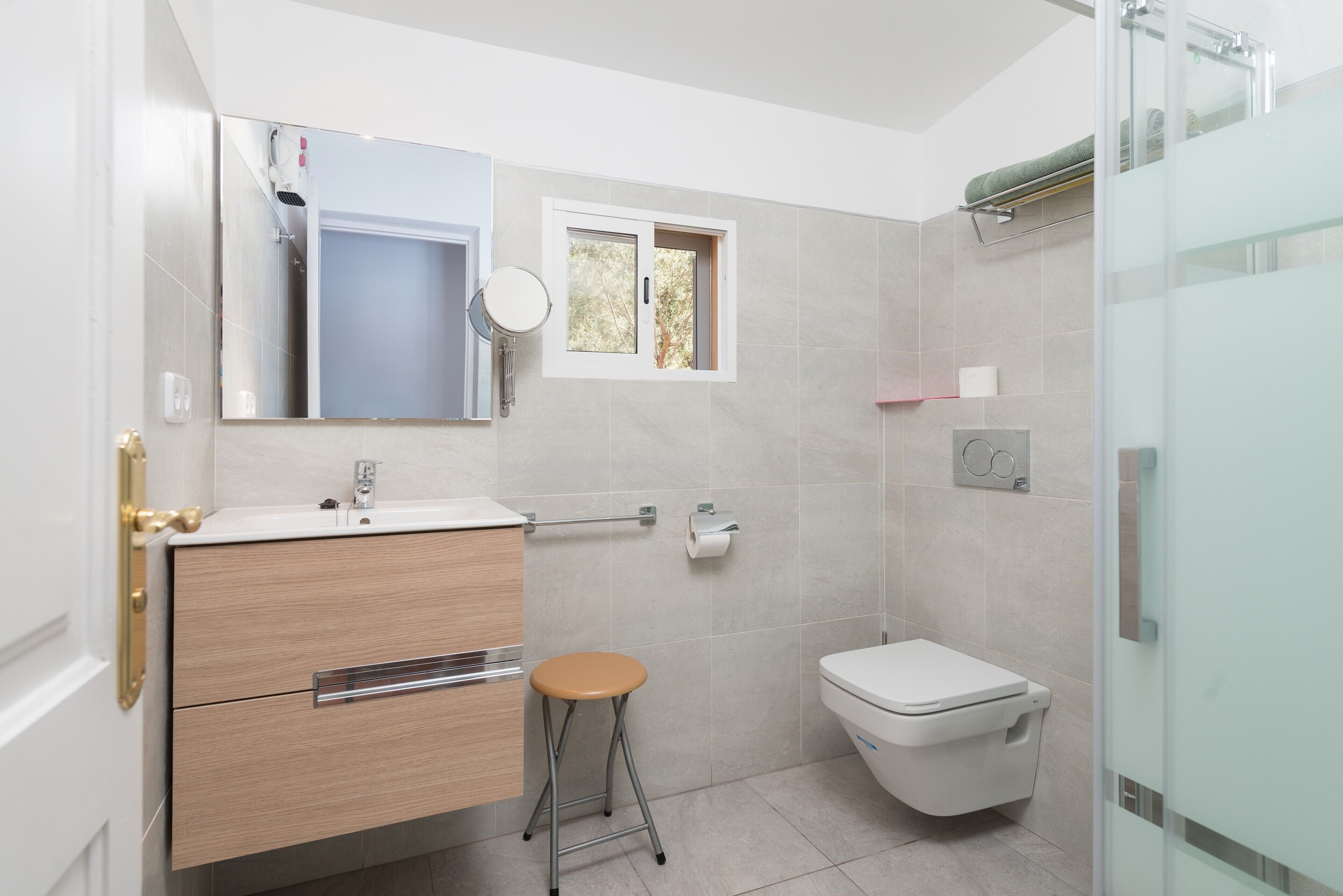Un baño moderno con inodoro, lavabo, espejo y un taburete pequeño.
