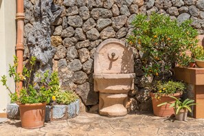 Un mur de pierres avec une fontaine en pierre rustique et des plantes en pot.