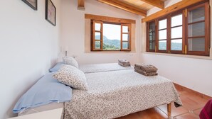 A bedroom with two beds, wooden beams, a window with a view, and a framed picture on the wall. - Stunning Mountain Views and Pool – Villas Ca'n Tamany & Ca'n Baixo (soller)