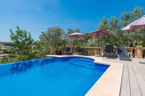 Une piscine entourée d’arbres et de bâtiments, avec des chaises longues et des parasols.