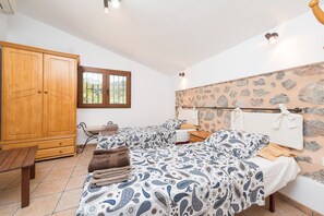 Une chambre avec deux lits, une armoire en bois, un banc et un mur en pierre.