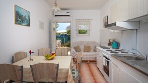 A compact kitchen with a dining area, a small stove, and a window overlooking a garden. - A 2  apt near beach w patio, parking and grill (Stobrec)