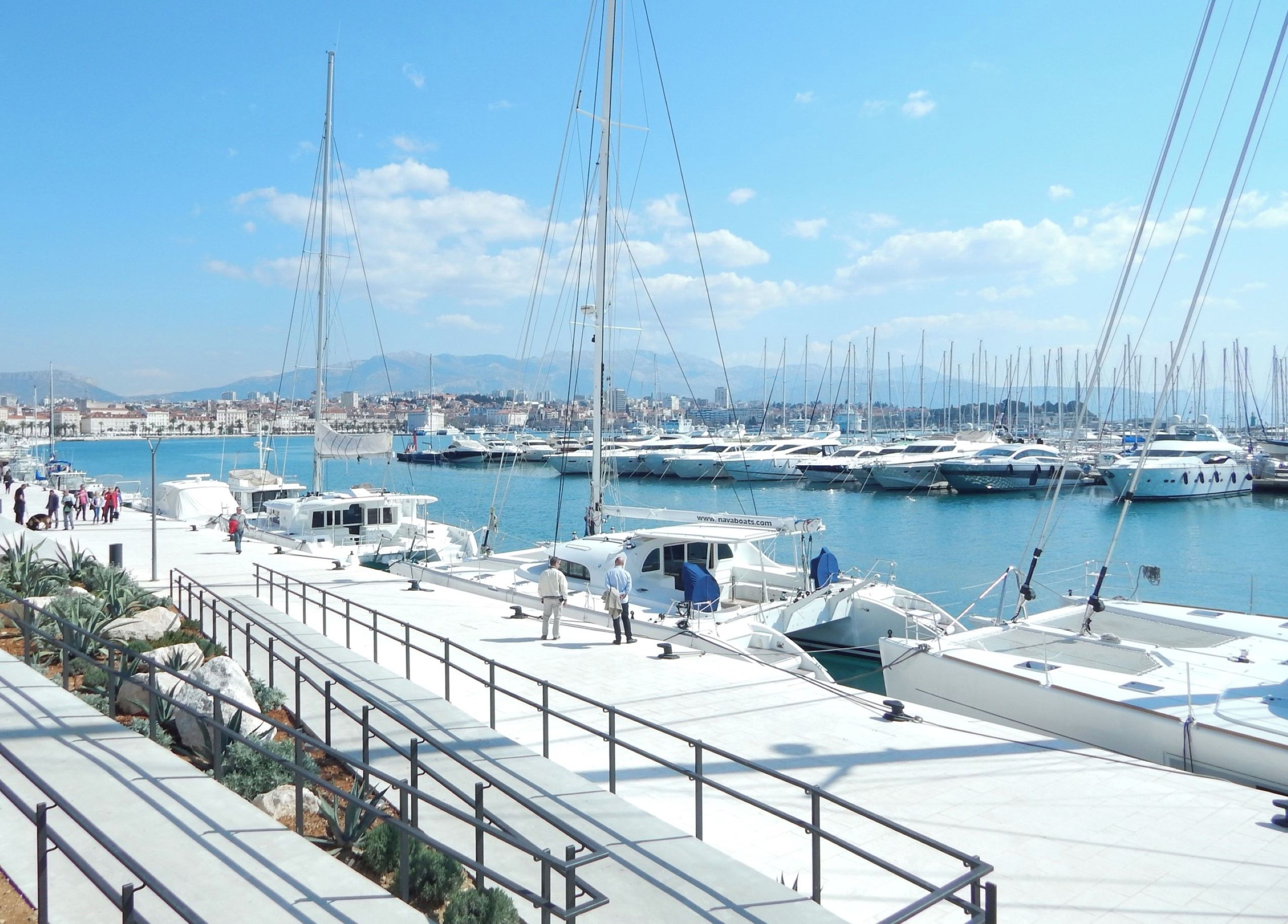 A marina with boats docked, a cityscape in the background, and a clear sky.