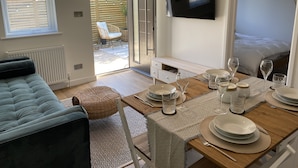 Un salon moderne avec un canapé, une table à manger pour quatre personnes et un téléviseur fixé au mur.