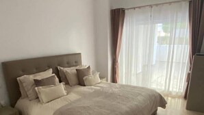 Een slaapkamer met een groot bed, een nachtkastje, een vloerkleed en een raam met gordijnen.