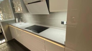 Een moderne keuken met een ingebouwde kookplaat, witte kastjes en een betegelde achterwand.