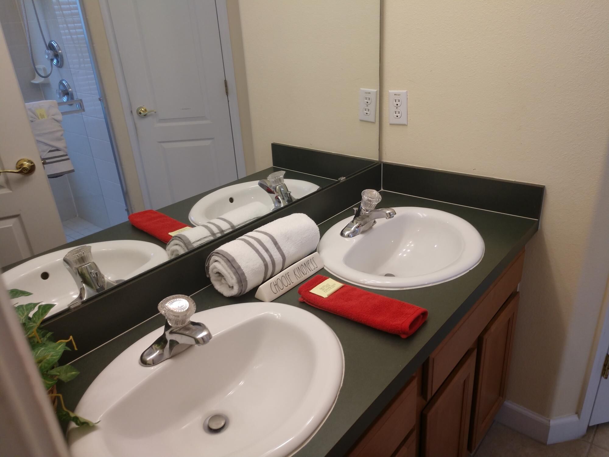 Un baño con dos lavamanos, un espejo y una ducha. Hay toallas y un paño rojo en la encimera.