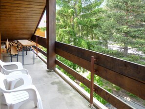 A covered outdoor area with a wooden table and chairs, a view of trees, and a metal railing.