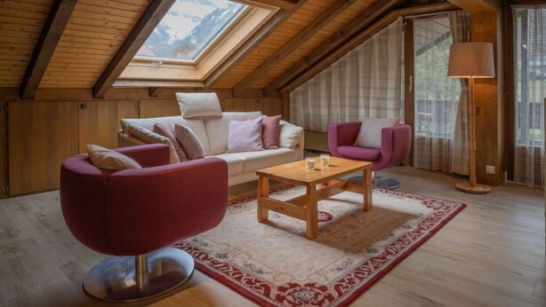 Une pièce mansardée chaleureuse avec un plafond en bois, un canapé, un fauteuil, une table et une lampe.