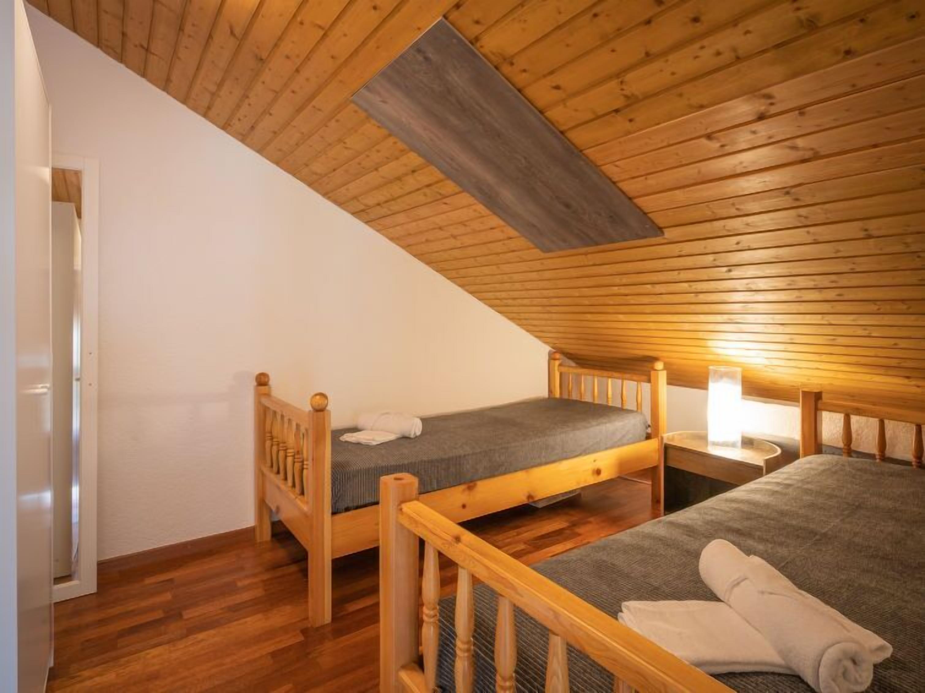 Une petite pièce chaleureuse avec deux lits en bois, un plafond en bois et une porte blanche.
