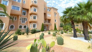 A multi-story building with a beige facade, multiple balconies, and a landscaped garden with cacti and palm trees. - Residencial Jazmines by Interhome (Calpe/Calp)
