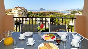 A balcony table set with breakfast items, a flower vase, and a scenic view of buildings and mountains. - Residencial Jazmines by Interhome (Calpe/Calp)