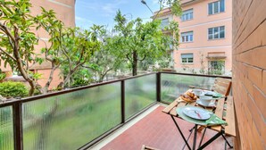 Ein Balkon mit Esstisch, umgeben von einem Metallzaun und Grünpflanzen.