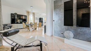 Ein modernes Wohnzimmer mit Lounge-Sessel, Essbereich und einer Küche im Hintergrund.