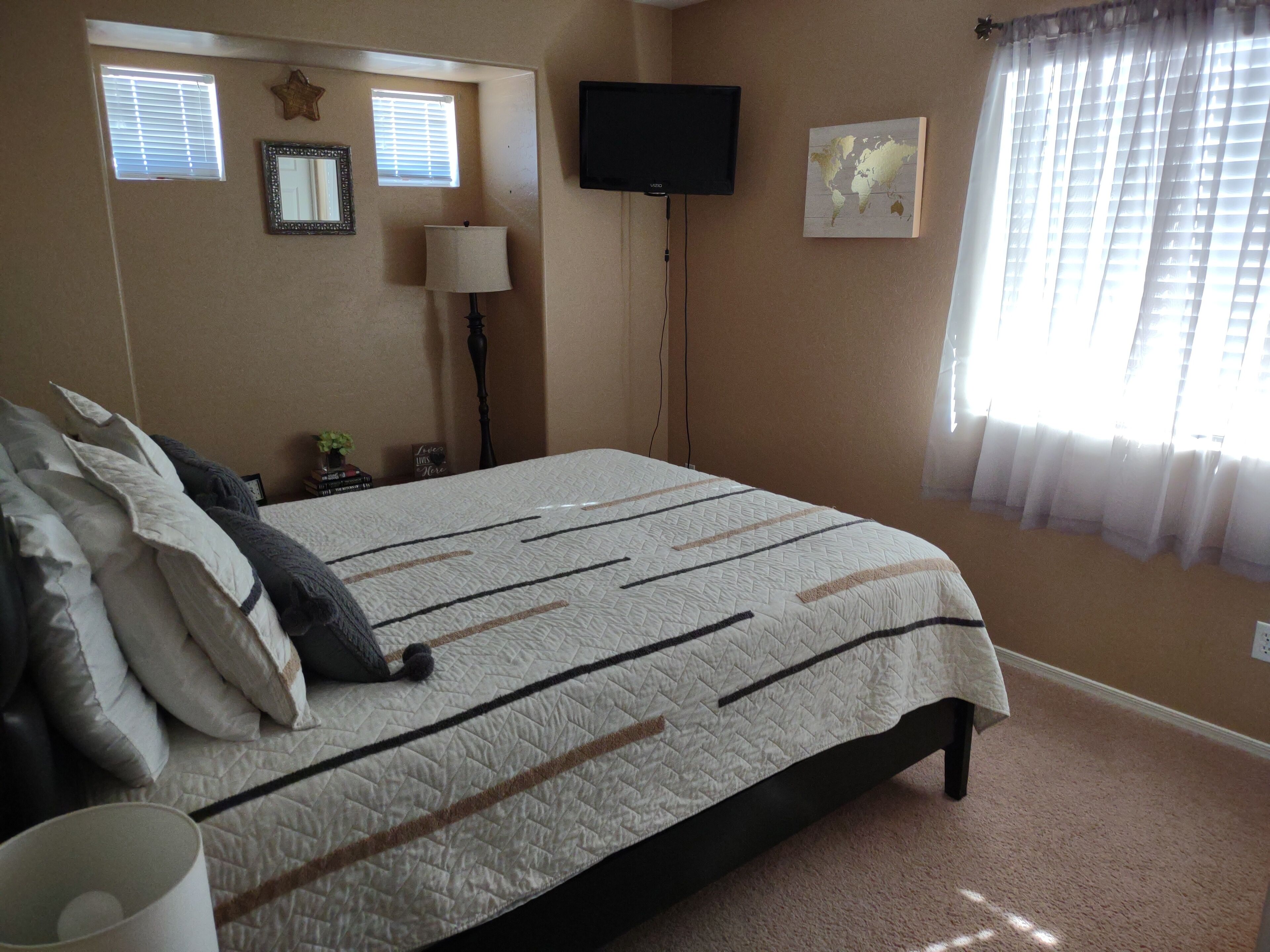 A bedroom with a bed, a TV, a world map, and a window with blinds.