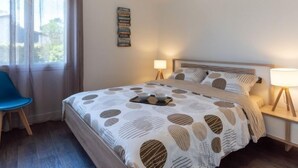 A neatly arranged bedroom with a bed, bedside lamps, a chair, and a bookshelf. - Les Trounques by Interhome (Mimizan)