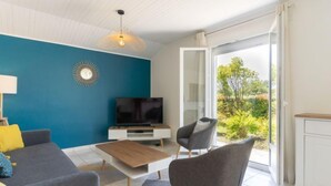 A modern living room with a blue accent wall, a flat-screen TV, a coffee table, and a seating area with a sofa and chairs. - Les Trounques by Interhome (Mimizan)