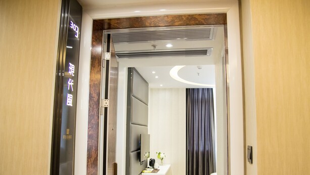A modern hotel room with a wooden door, a flat-screen TV, a small table with a vase, and a large window with curtains. - Ai Luo Si (Guangzhou)