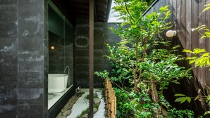 Une salle de bain moderne avec une baignoire sur pieds, une douche séparée par des parois en verre et un petit jardin agrémenté d’une clôture en bois et de verdure.