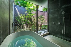 A modern bathroom with a freestanding bathtub, a glass shower enclosure, and a view of a garden through a large window. - Soushuku Machiya House (Kyoto)