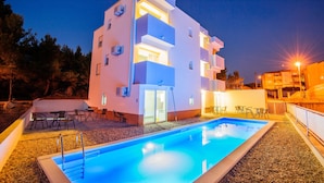 A modern building with a swimming pool, outdoor seating, and a well-lit entrance.