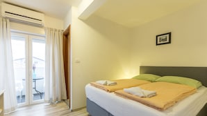 A hotel room with a bed, a window with curtains, a picture on the wall, and a view of the outside.