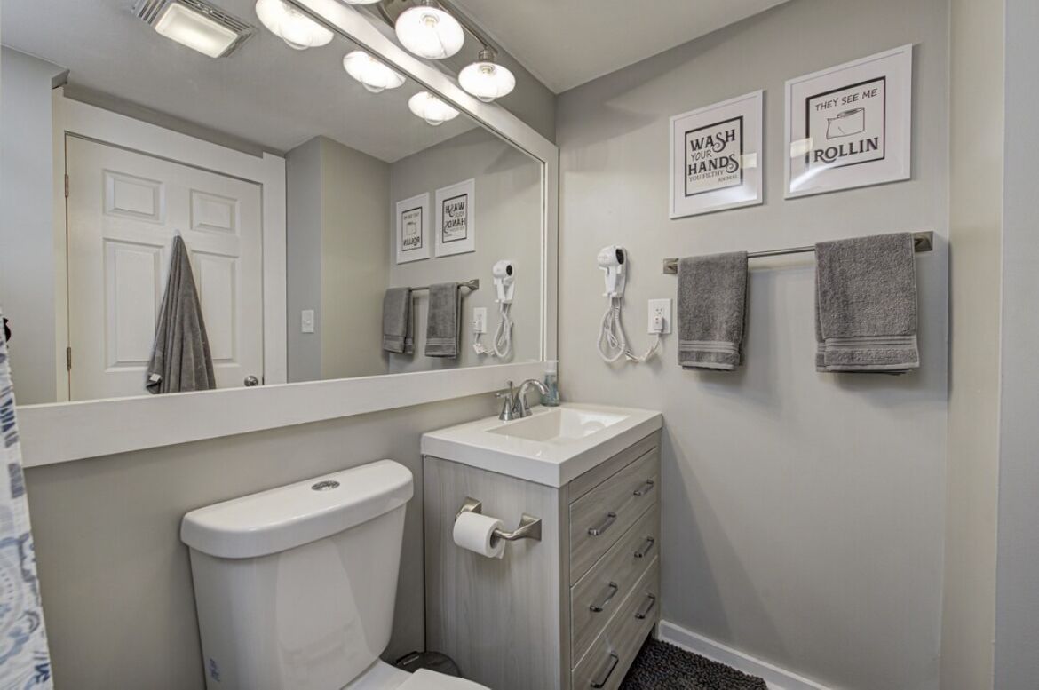 A bathroom with a toilet, sink, vanity, and towel racks.