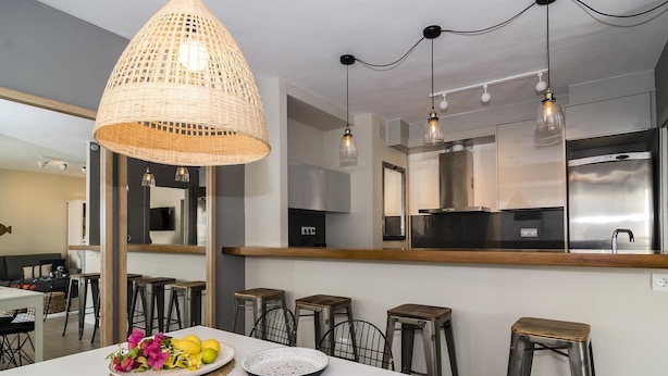Uma cozinha moderna com bancada branca, eletrodomésticos de aço inoxidável e luminária pendente.