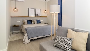 Quarto moderno com cama, mesas de cabeceira, abajur e sofá.