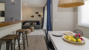 Cozinha moderna com bancada branca, dois bancos e uma mesa de jantar com um prato de limões e flores.