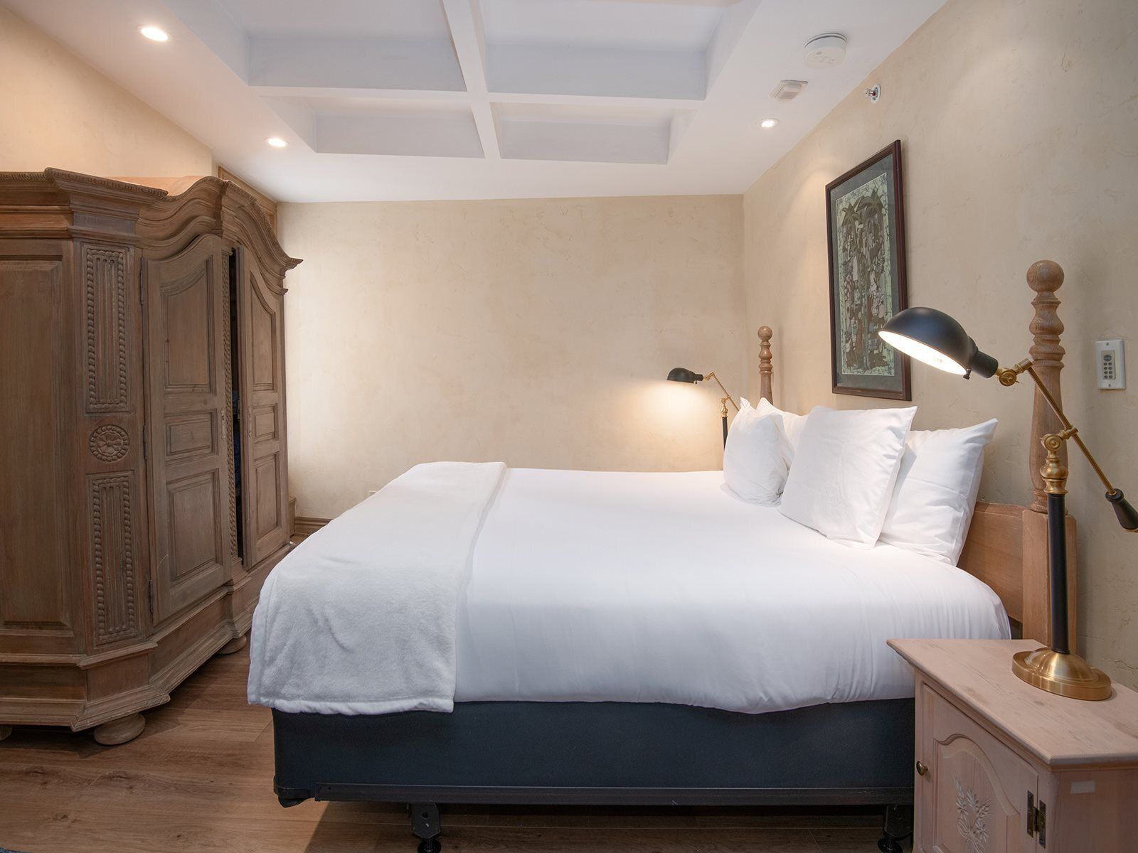 A neatly made bed with white linens, a wooden nightstand with a lamp, and a large wardrobe.