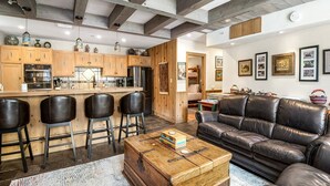 Una cocina moderna con armarios de madera, un refrigerador de acero inoxidable y una barra con taburetes.