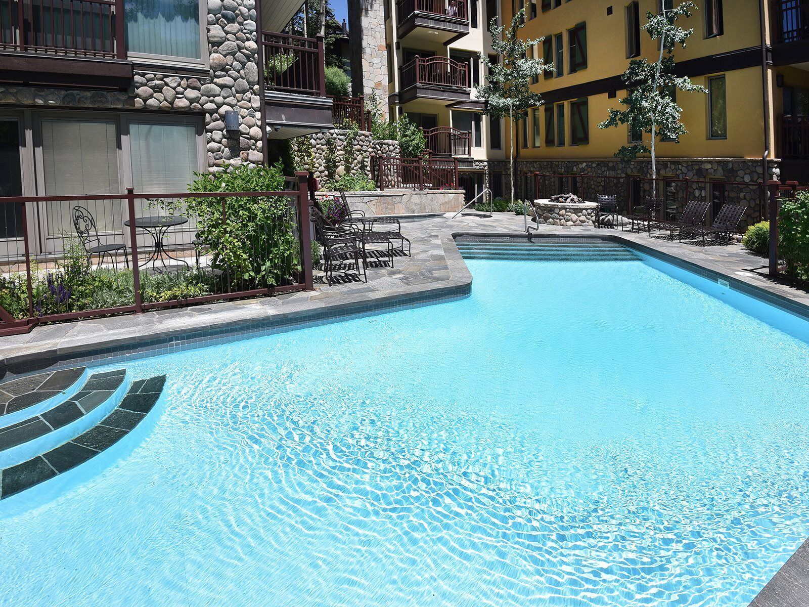 Piscina com borda de pedra, rodeada por área de estar ao ar livre e uma parede de pedra.
