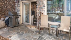 Un patio de piedra con una parrilla y mobiliario de exterior.