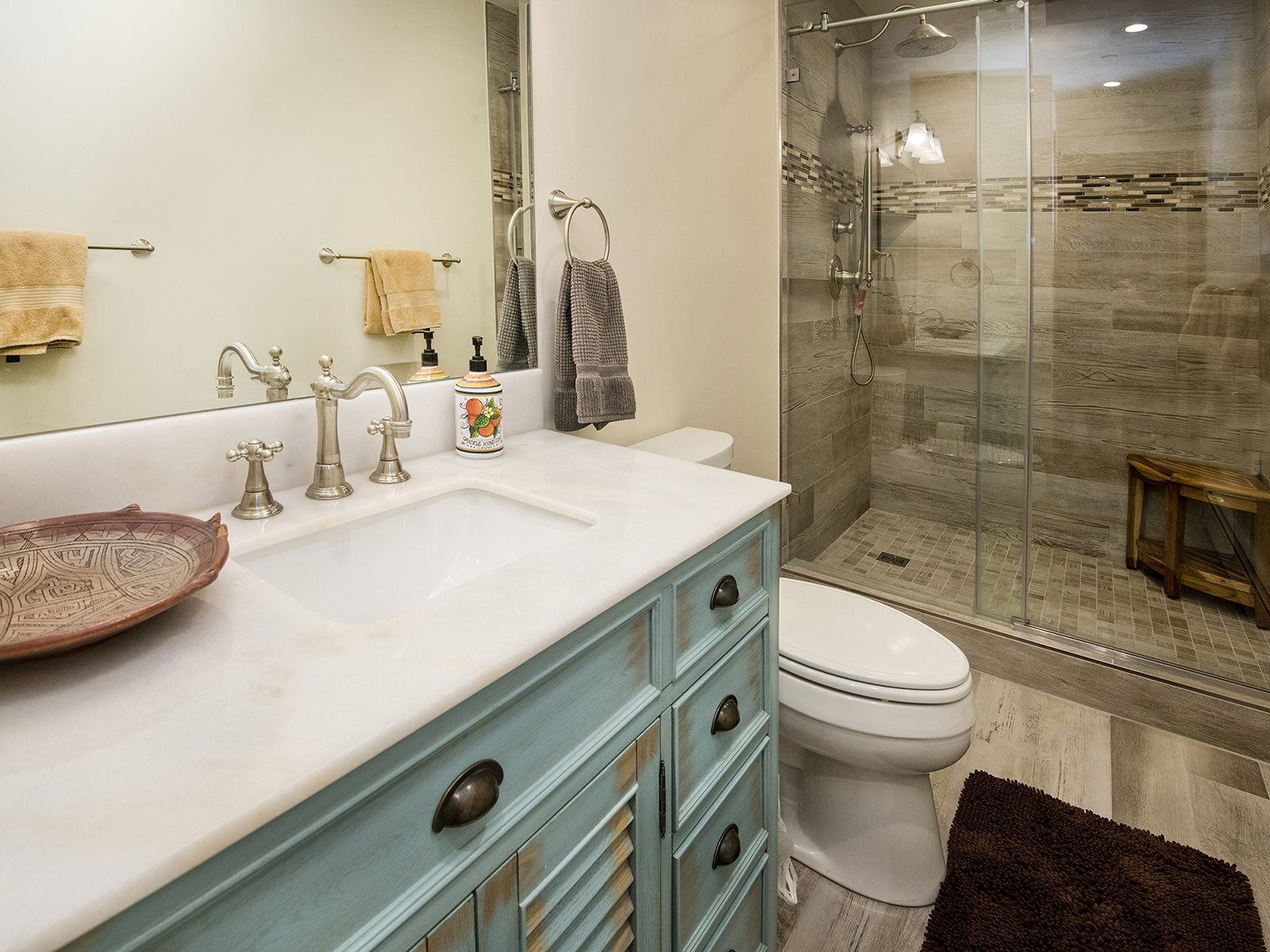 Une salle de bain dotée d’un grand miroir, d’un lavabo à deux robinets, de toilettes et d’une douche à parois de verre.