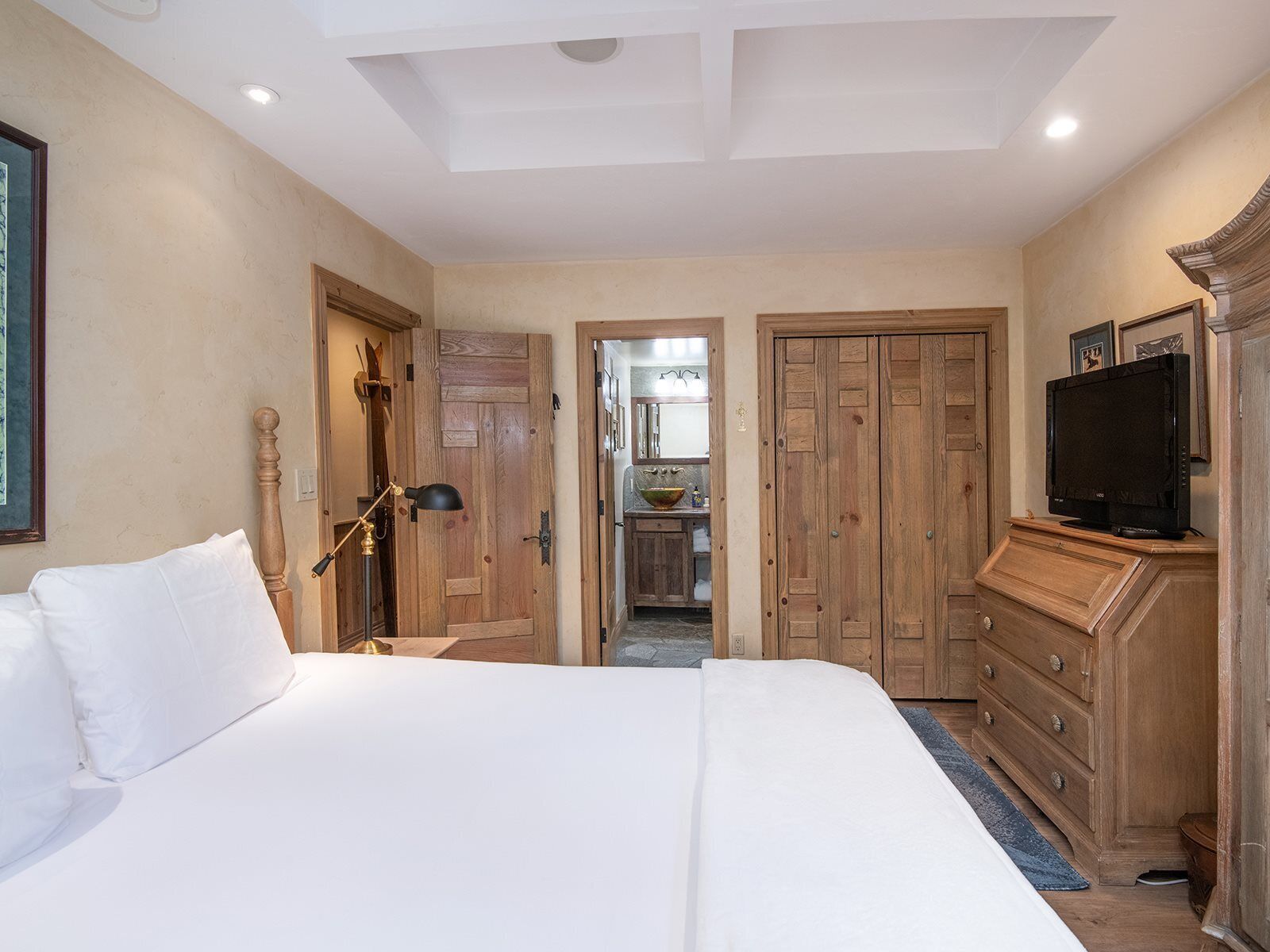 A bedroom with a large bed, wooden wardrobe, and a television.