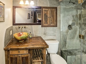 A bathroom with a rustic wooden vanity, a large bowl sink, a white toilet, and a glass-enclosed shower. - Village Center Condo 1F (Vail)