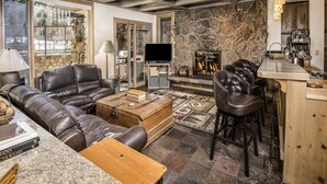 Una sala de estar acogedora con sofás de cuero, una chimenea de piedra, un televisor y una zona de bar.