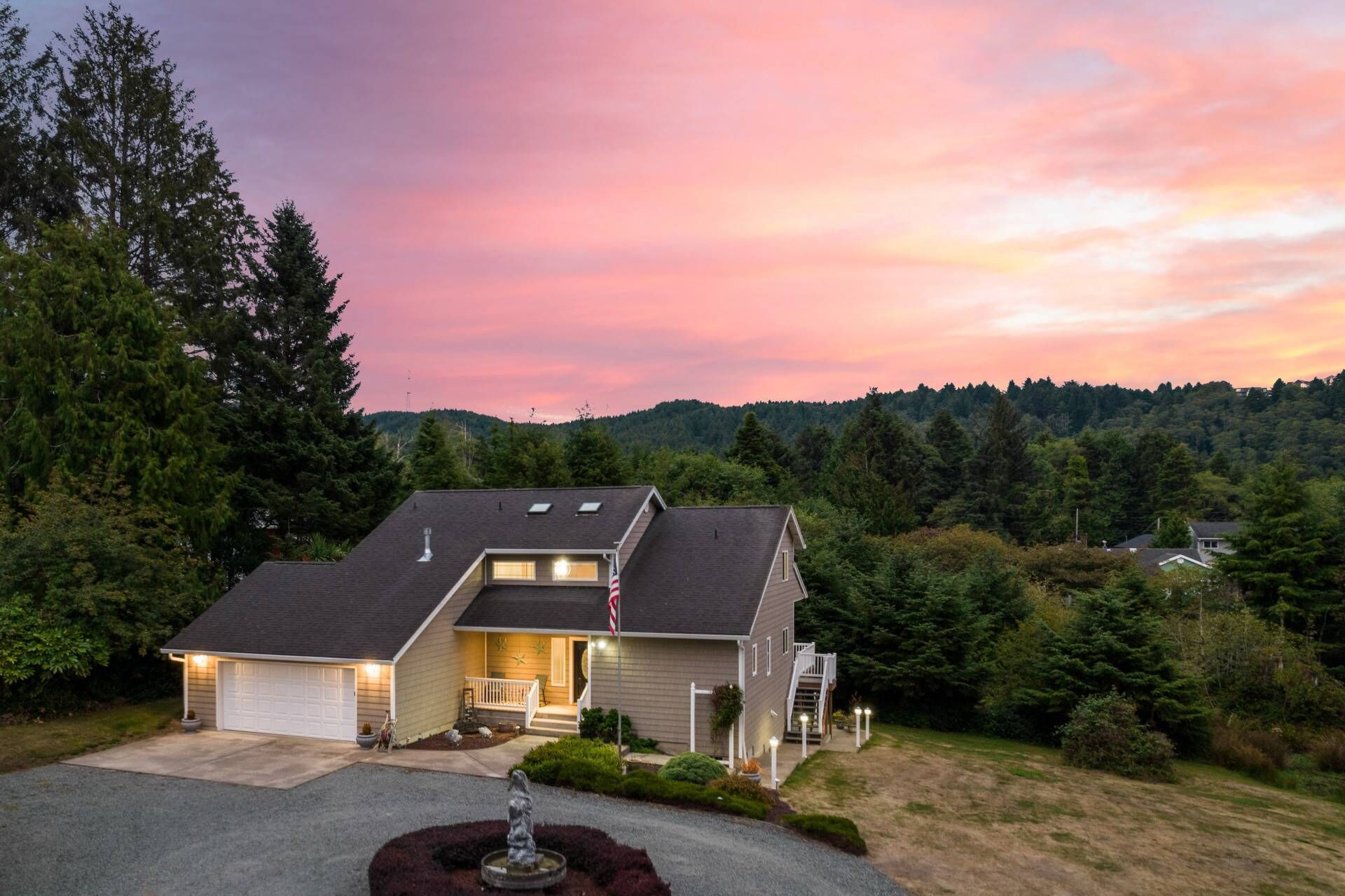 A two-story house with a garage, a covered porch, and a landscaped front yard with a fountain.