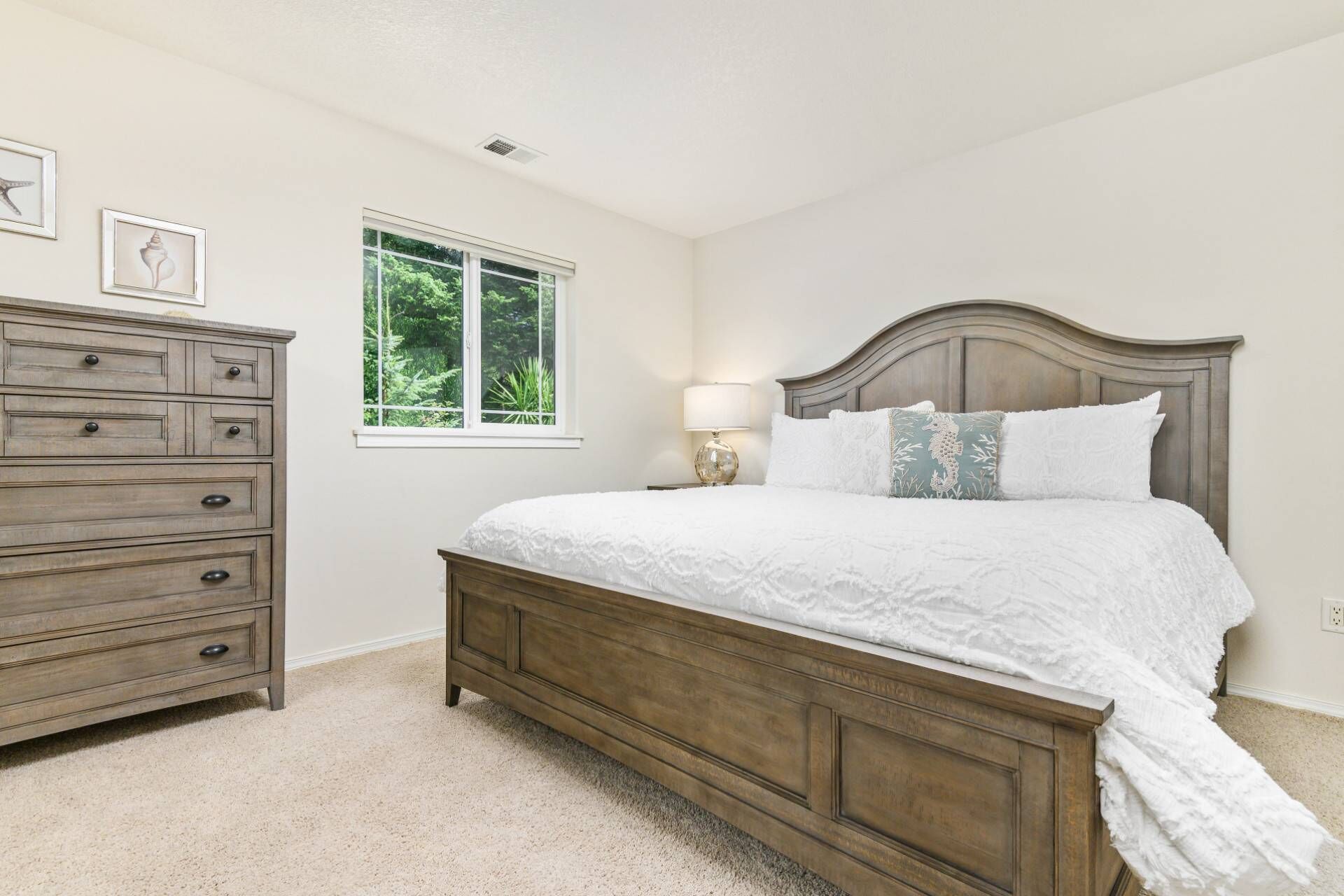 A bedroom with a wooden bed, a dresser, and a window with a view of greenery.