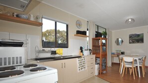 A kitchen with a stove, cabinets, a window, a sink, and a dining area with chairs and a table. - Relaxed, beachy 2 bed apartment, only 1.9kms from the beach, close to shops (Kingscote)