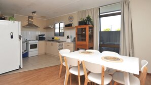 A compact kitchen with white appliances, a dining table with chairs, and a large window with curtains. - Relaxed, beachy 2 bed apartment, only 1.9kms from the beach, close to shops (Kingscote)