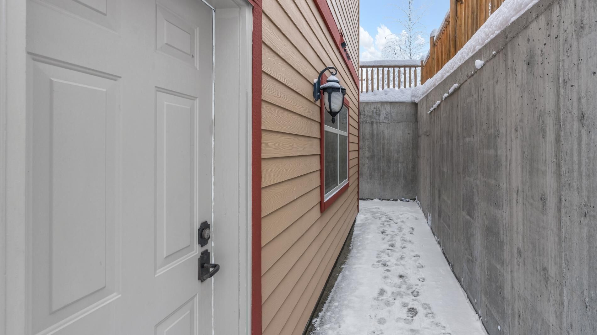 Un étroit couloir extérieur avec une porte blanche, un revêtement de façade beige et un mur en béton.