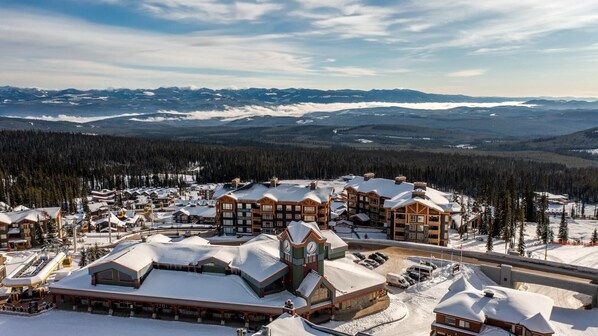 A snow-covered resort with multiple buildings, a ski lift, and a mountainous backdrop.