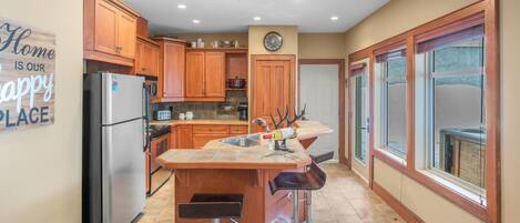 A modern kitchen with wooden cabinets, a stainless steel refrigerator, and a large island with bar stools.