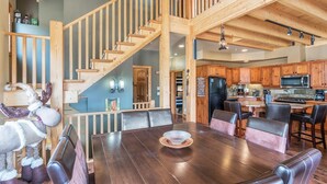 Une cuisine moderne avec des meubles en bois, un réfrigérateur en acier inoxydable et un coin repas comprenant une table en bois et des chaises en cuir.