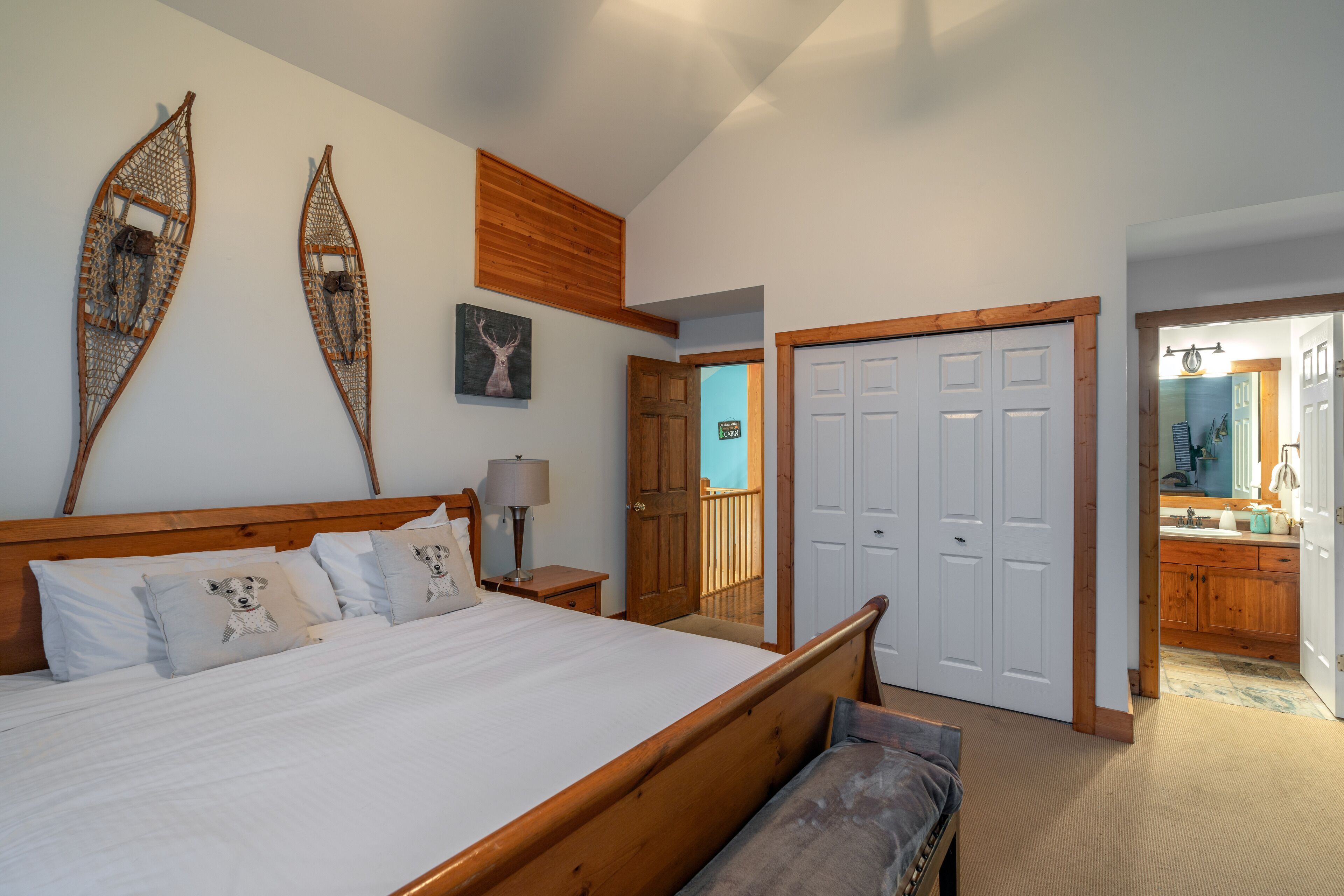 A bedroom with a wooden bed, a nightstand, a lamp, a door leading to a balcony, and a bathroom visible through an open door.