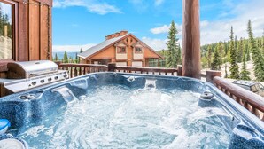 Un bain à remous avec une terrasse en bois, un barbecue et un chalet en arrière-plan.