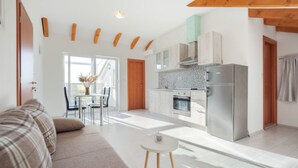 Una sala de estar moderna con un sofá, una mesita redonda y una zona de cocina con armarios y electrodomésticos.